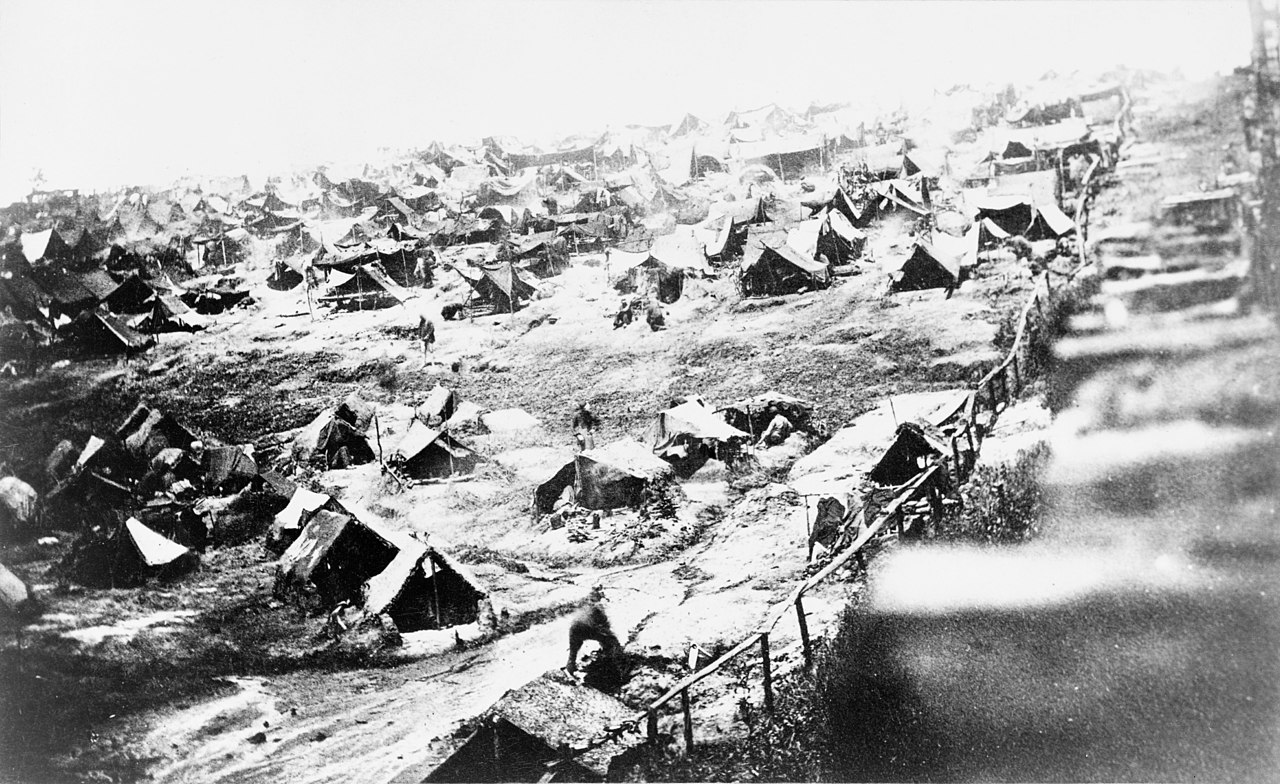 Tents in muddy ground next to prison fence.