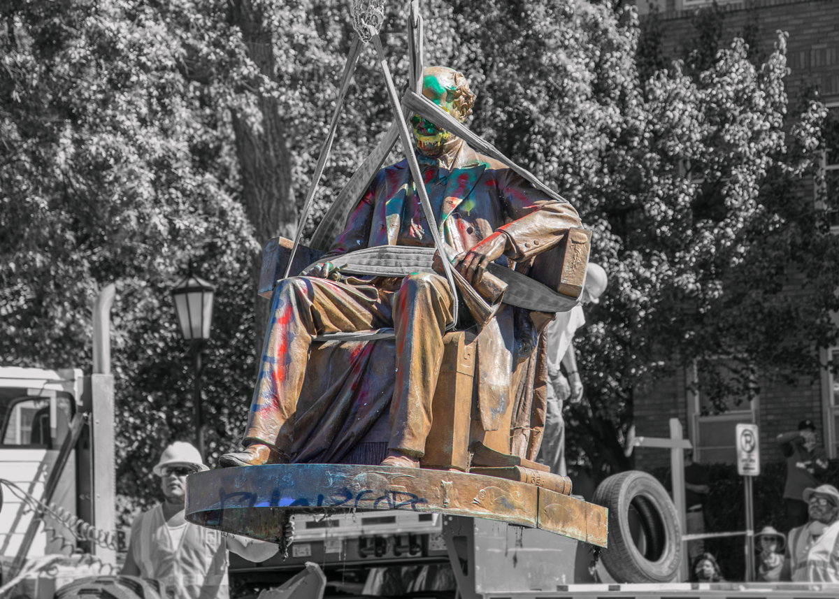 A graffitied Matthew Fontaine Maury Monument from Richmond's Monument Ave, being lifted by a crane for removal.