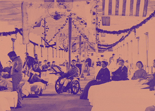 A Ward in Armory Square Hospital, Washington, D.C. U.S. soliders are lying in beds against the walls and one soldier is in a wheelchair in the center of the image. Two women nurses are seated next to bedridden soliders on the right. The ward's ceiling is decorated with streamers and U.S. Flags.